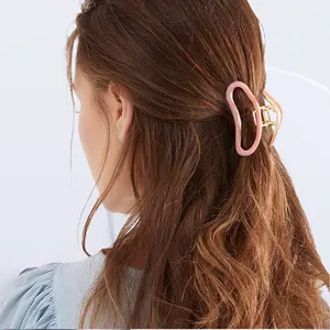 Détail d'une pince à cheveux en résine rose et base dorée sur une coiffure demi-queue
