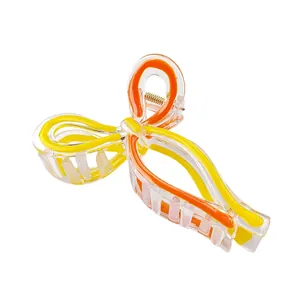 Détail d'une pince à cheveux transparente avec des motifs courbés jaunes et oranges
