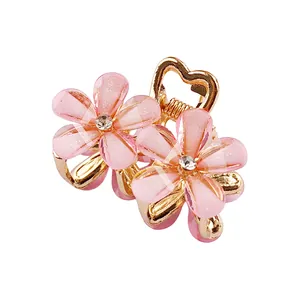 Vue détaillée de pinces à cheveux à fleurs en résine rose avec coeurs dorés et strass
