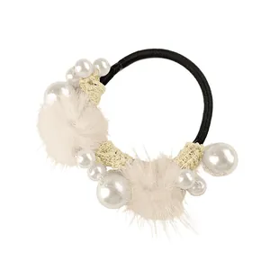 Detailed close-up of hair tie with soft cream fur pom poms and elegant white pearls