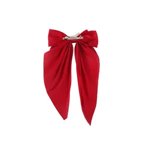Detailed close-up of a large red satin bow hair clip with long elegant hanging ribbons