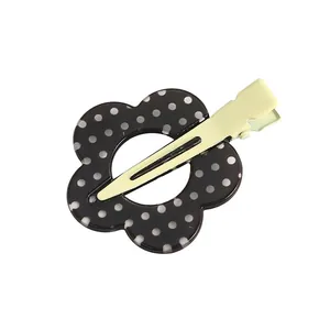Detalle de una pinza para el pelo con forma de flor y lunares blancos en clip de metal verde