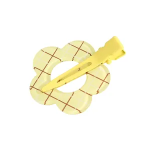 Detalle de pinza para el pelo con flor amarilla, estampado de cuadros y base mate