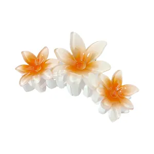Detailed view of three gradient orange plumeria flowers on a white hair claw clip