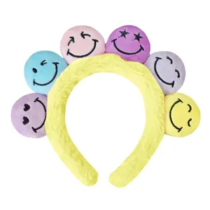 Nahaufnahme von flauschigem gelbem Plüschstirnband mit sechs bunten Smiley-Gesicht-Bällen