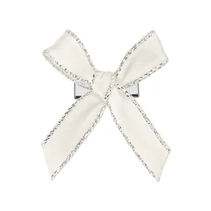 Détail du nœud papillon en satin crème avec bords pailletés et pince crocodile en métal