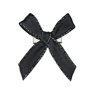Détail d'une pince à cheveux nœud noir avec bords pailletés argentés et clip métal