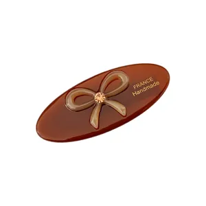 Detail einer ovalen Acetat-Haarklammer mit kleiner Schleife, Strass und Handmade-Aufdruck