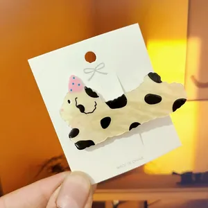 Close-up of a cream-colored spotted dog hair clip made of premium acetate on a display card
