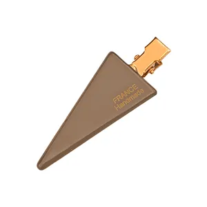 Detail of mocha brown triangular hair clip with gold metal finish and handmade script