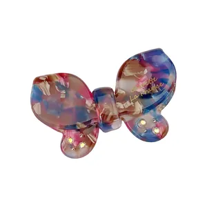 Detailed close-up of a bow-shaped acetate hair clip with rhinestones and elegant gold text