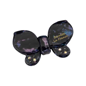 Macro detail of acetate butterfly hair clip with gold text and small rhinestones