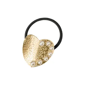 Detalle de goma para el pelo con corazón dorado martillado y perlas sobre fondo blanco