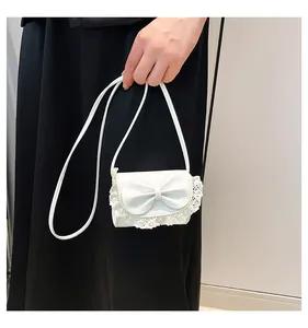 Detail of white mini bag with lace trim and large bow accent on leather surface