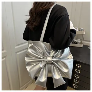 Dettaglio della borsa tote argentata con fiocco metallico indossata a spalla su modella