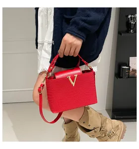 Detail view of red textured leather handbag with gold V hardware and adjustable strap