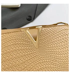 Detailed close-up of beige woven texture and gold V-shaped metal logo on handbag