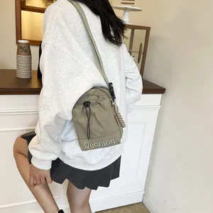 Olive green nylon drawstring crossbody bag worn by a model in a casual cafe setting