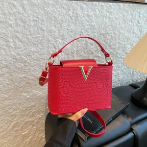 Sac à main chic rouge à texture tissée et boucle en V dorée porté en bandoulière