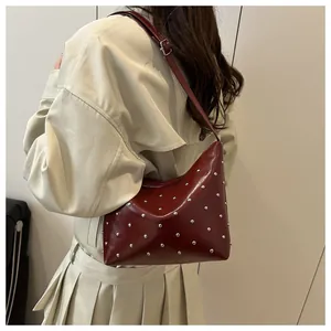 Detail of a dark red hobo bag with silver rivets worn over a khaki trench coat