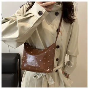 Detail view of brown glossy leather crossbody bag with silver rivet studs and long strap