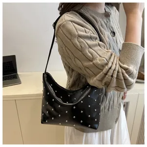 Model wearing a black leather crescent shoulder bag with silver stud accents and thin straps