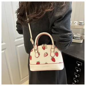 White shell bag with strawberry pattern shown as a crossbody on a female model