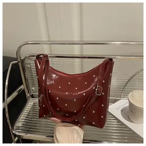 Close-up of wine red glossy faux leather shoulder bag with silver rivet details