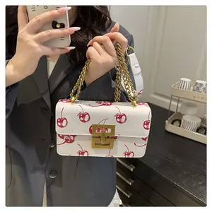 Detail of a white crossbody bag with red cherry prints and a golden chain strap