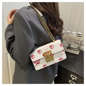 Detail of white cherry print shoulder bag with gold chain strap on a grey suit jacket