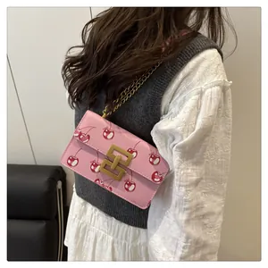Pink crossbody square bag with cherry print and golden chain strap on a model