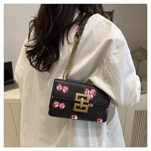 Detail view of small square crossbody bag with cherry print and golden chain strap