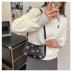 Detailed view of black faux leather underarm bag with red cherry prints and gold hardware
