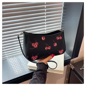 Close-up of vibrant cherry print on black leather shoulder bag with gold metal link