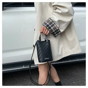 Détail de la texture tressée noire du mini sac bandoulière avec plaque en métal argenté
