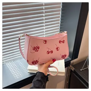 Detailed view of a pink shoulder bag with red cherry prints held by hand in a chic setting