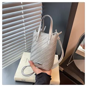 Détail de la texture tressée argentée sur un mini sac à bandoulière et plaque métal