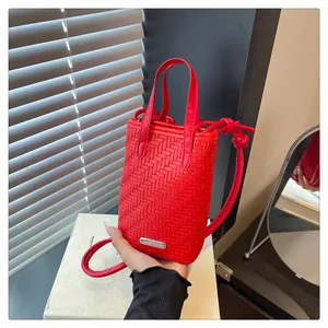 Détail du mini sac tressé rouge avec bandoulière à nœud et plaque de logo argentée