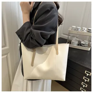 Minimalist beige tote bag with brown leather straps shown on shoulder in office setting