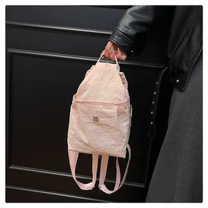 Detail of light pink nylon mini backpack featuring a drawstring and metal button pocket
