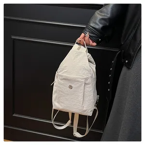 Close-up of off-white crinkled nylon backpack featuring a silver circular metal logo detail