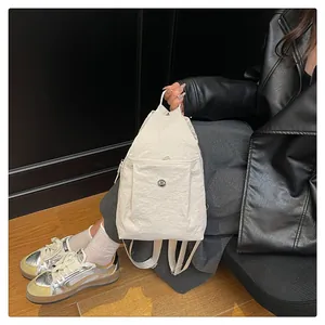 Detail of white wrinkled nylon backpack showing front zipper pocket and metal button accent