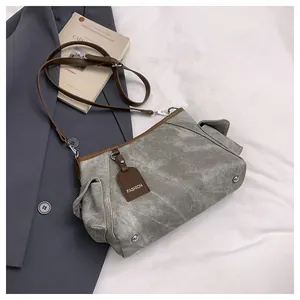 Detail of grey canvas crossbody bag with brown leather trim and metal bottom studs