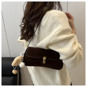 Détail du sac à bandoulière en daim marron foncé avec fermoir doré et breloques