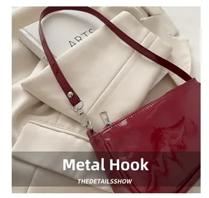 Close-up of silver metal hook and dark red patent leather strap on shoulder bag