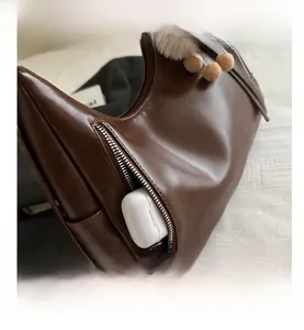 Close-up of brown leather tote bag side pocket with keychain and wireless earphone case