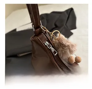 Detail of dark brown leather tote bag with silver zipper and khaki plush pompom charm