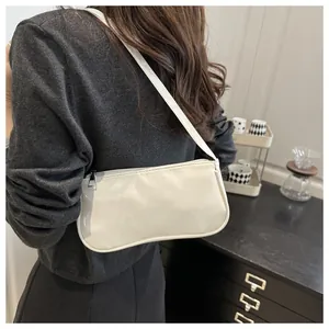 Side view of a glossy white patent leather baguette bag styled over the shoulder by a model
