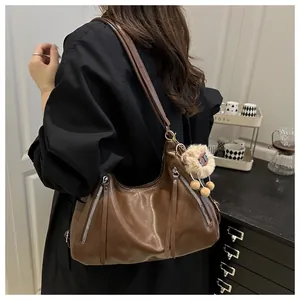 Detailed view of brown faux leather tote bag with silver zippers and plush ball charm