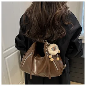Detail of dark brown leather hobo bag featuring metal zippers and a plush lion charm